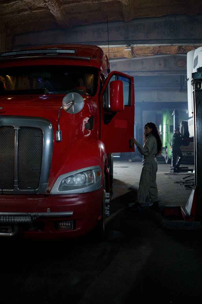 A female mechanic working on a red truck inside a dimly lit garage, focusing on automotive repair.