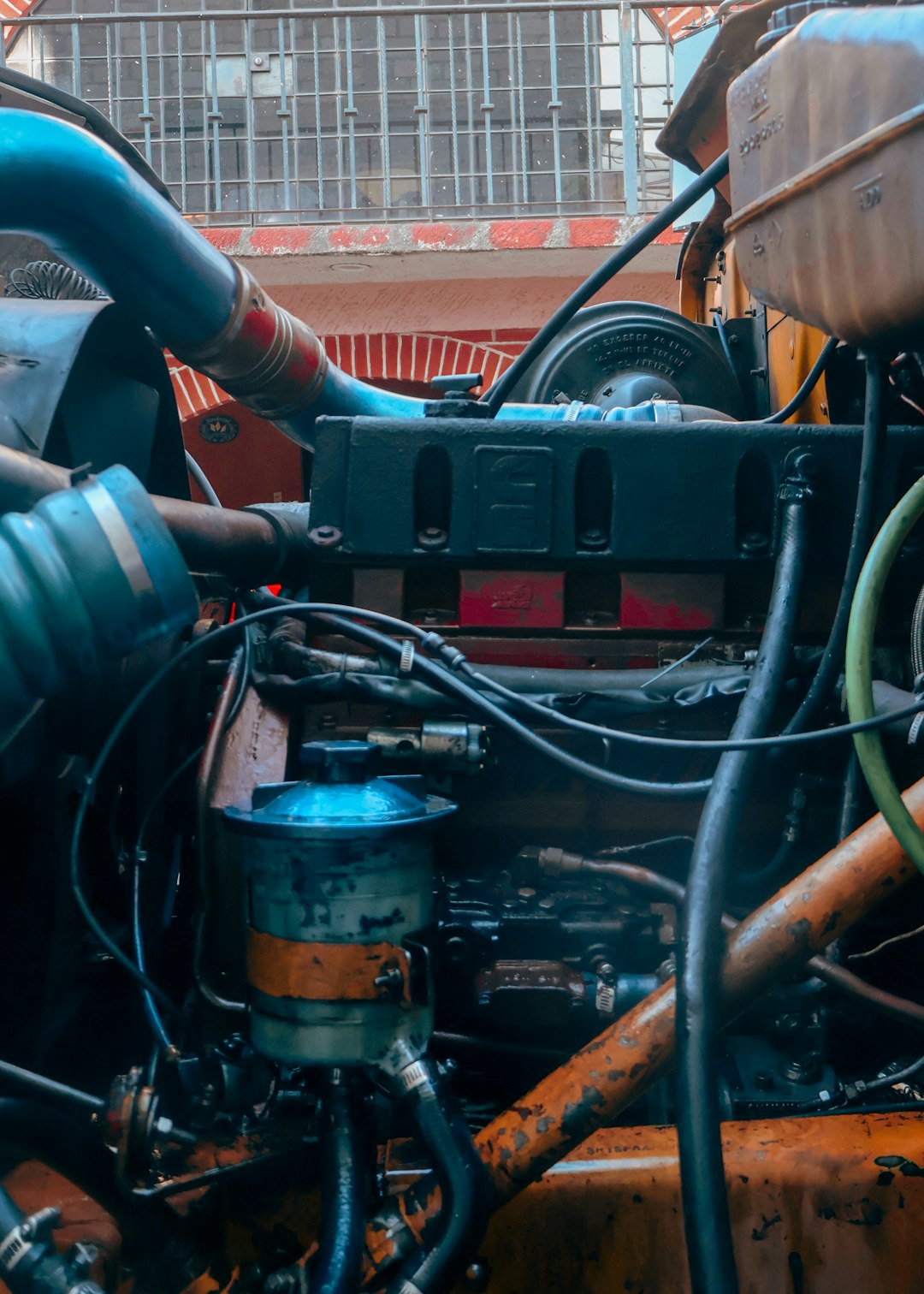 Primer plano del motor de un camión industrial con mangueras, filtros y piezas metálicas desgastadas. La mezcla de texturas, grasa y color revela la mecánica interna de la maquinaria pesada, transmitiendo fuerza, trabajo y vida cotidiana en el entorno del transporte y la industria.