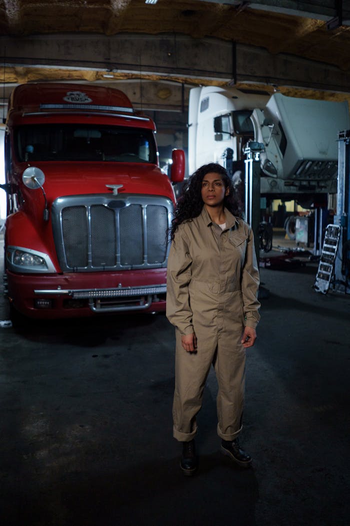 A mechanic wearing a jumpsuit stands confidently in a garage with a red truck.